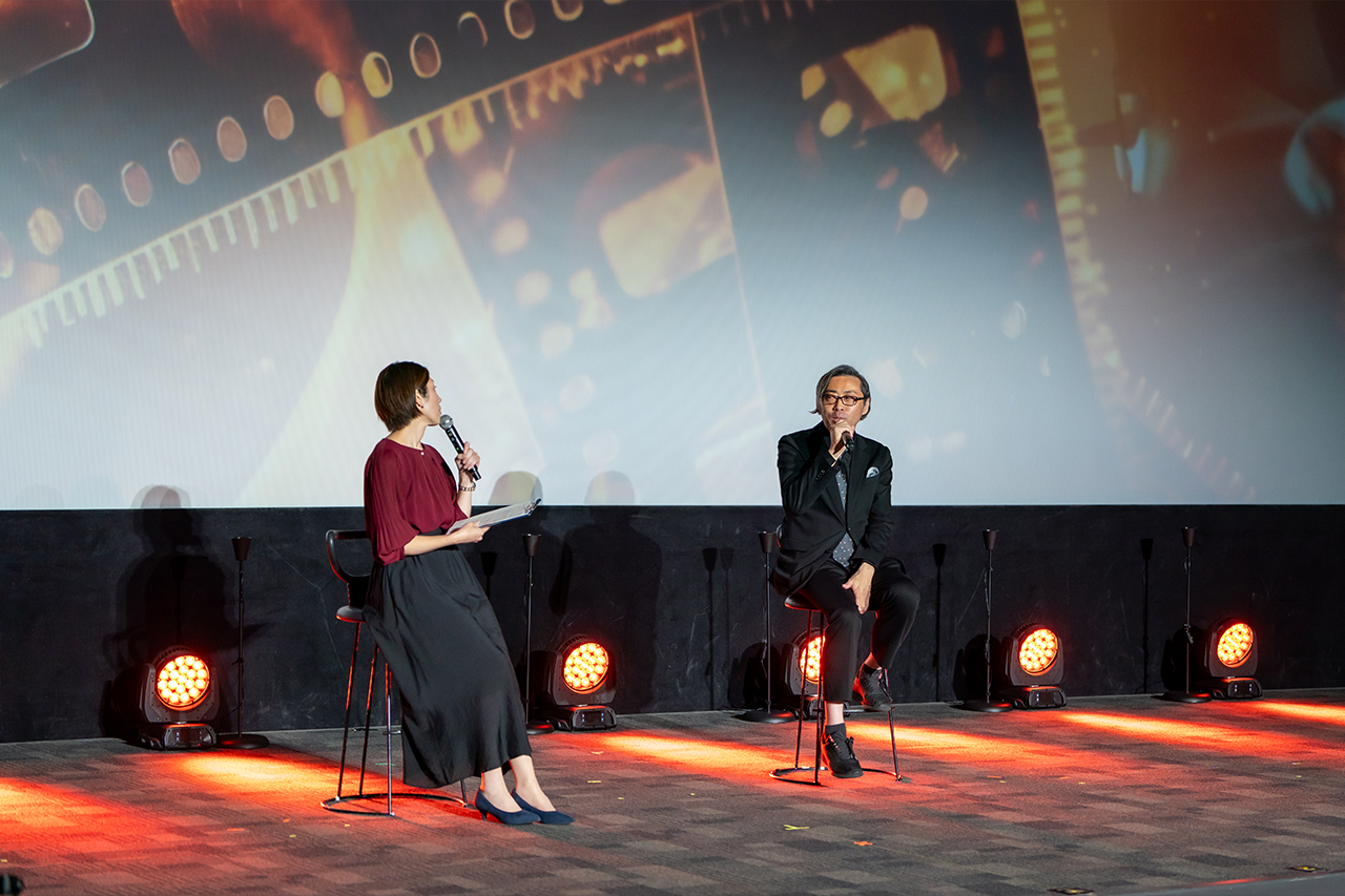 壇上で話す（左から）MCと齋藤優一郎プロデューサー